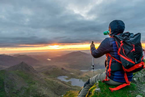A person sitting on a rock. we can see a panorama view of the maountains and lochs in the distance
